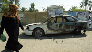 An Iraqi woman passes a burnt car on the site where Blackwater guards opened fire in western Baghdad.