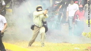 A state police photo appears to show a masked man firing a handgun Tuesday at unarmed demonstrators.