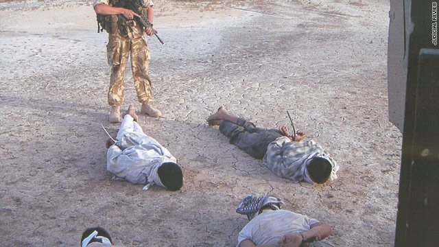 An armed soldier stands over prisoners face down on the ground with their hands bound.