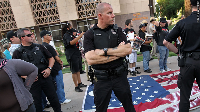 Police stand guard over a flag made by immigrant rights supporters as conservatives listen to speeches July 31 in Phoenix.