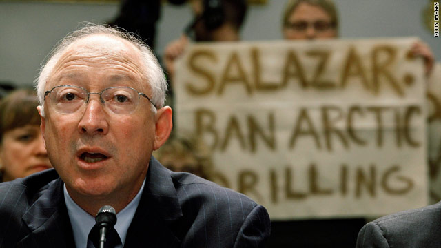 Protesters hold a sign behind Interior Secretary Ken Salazar as he testifies Wednesday before a congressional committee.