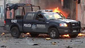 A police truck is parked in front of the remains of a car that exploded in a bombing in Juarez, Mexico, earlier this month.