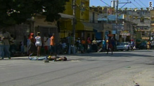 People walk by a gruesome scene Friday -- a man facing up, with arms out -- on John Brown Avenue after a mob left.