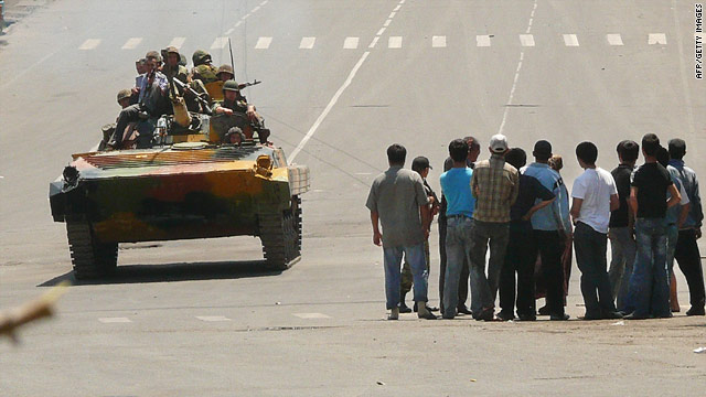 Kyrgyz soldiers on an armored vehicle drive past a group of people in Osh on June 11, 2010