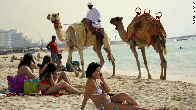 An Emirati man riding a camel passes by foreigners sunbathing on a beach in Dubai last spring.