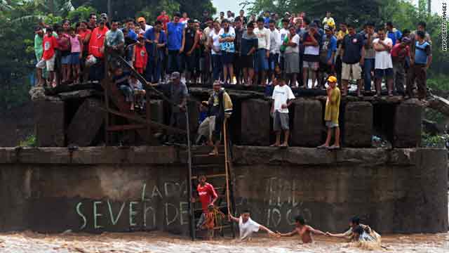 People try to cross the overflowed Huiza River, as others look from a damaged bridge in La Libertad, El Salvador.