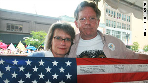 Lori and Jeff Wilfahrt attend their first gay pride parade. They hold a flag signed by their son's comrades.