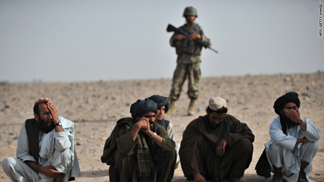 Villagers squat as an Afghanistan National Army soldier stands guard behind them, as unseen U.S. Marines search an abandoned compound belonging to an improvised explosive device maker in Sistani, Helmand Province, on May 12, 2011.