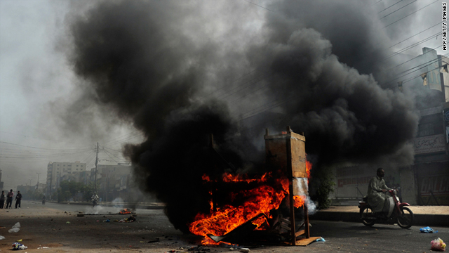 A motorcyclist rides past a pile of burning tires and furniture in a violence-hit neighbourhood of Karachi, Pakistan, on Friday.