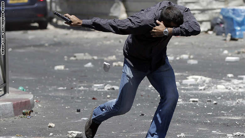 شرطي سري إسرائيلي يشهر سلاحه ويتقي حجارة المتظاهرين الفلسطينيين