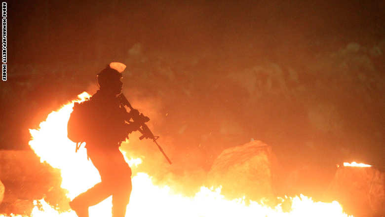 جندي إسرائيلي يجتاز إطارات أشعلها متظاهرون فلسطينيون في قلنديا