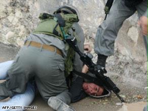 جندي إسرائيلي يقبض على شاب فلسطيني وآخر يراقبه