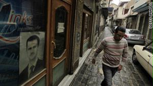 سوري يمشي في الشارع، بينما علقت صورة الرئيس السوري على واجهة أحد المحلات